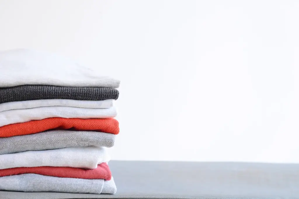 Stack of colorful folded shirts on gray table with empty space for text. Household concept.