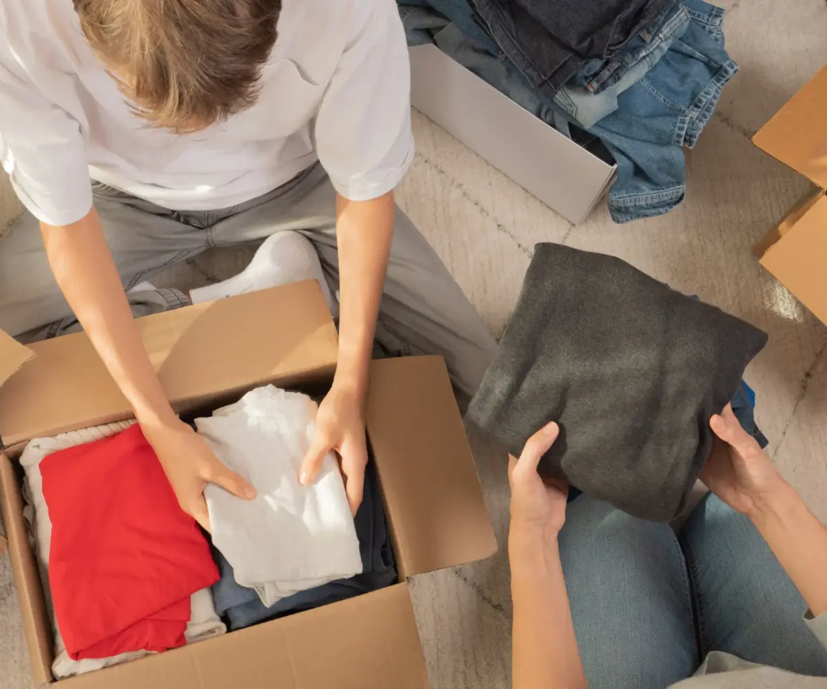 Woman and child sorting clothes and packing into cardboard box.