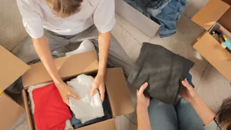 Woman and child sorting clothes and packing into cardboard box.